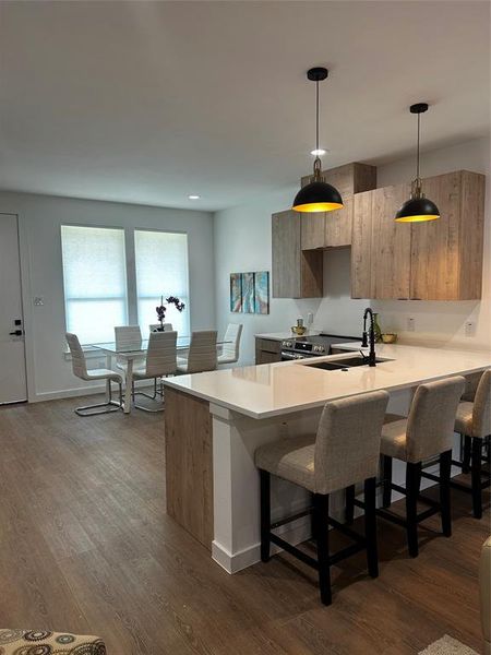 Kitchen featuring kitchen peninsula, hardwood / wood-style floors, sink, decorative light fixtures, and a kitchen bar