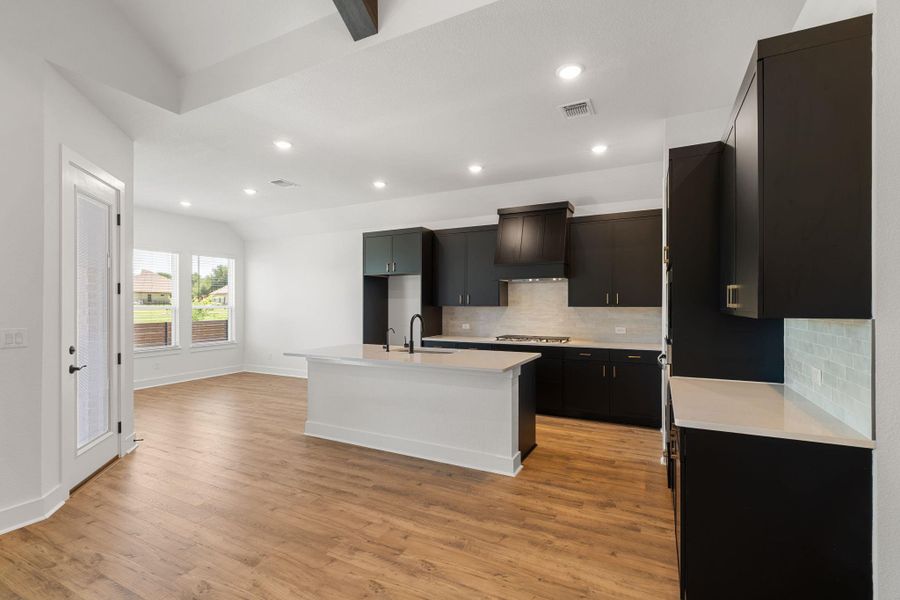A well-appointed kitchen featuring a substantial island, dark cabinetry, and integrated appliances seamlessly transitions into an airy living area.