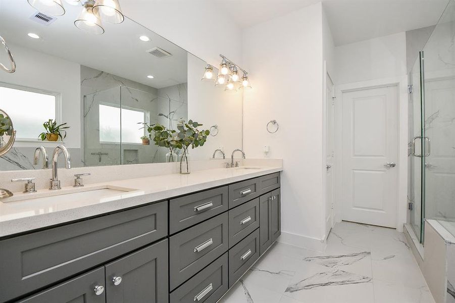 The en-suite bathroom off the primary bedroom is a modern design with double vanity, gray cabinets and large mirrors.