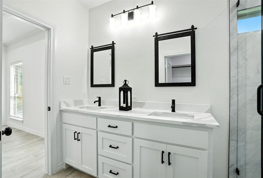 Full bath with double vanity, light wood finished floors, and a shower stall