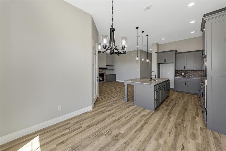 Kitchen with gray cabinetry, a chandelier, light stone counters, light wood-style flooring, and recessed lighting