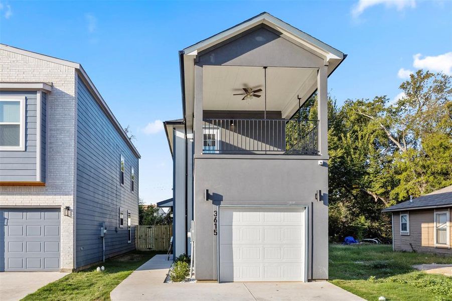 View of side of property with ceiling fan, a garage, a lawn, and a balcony