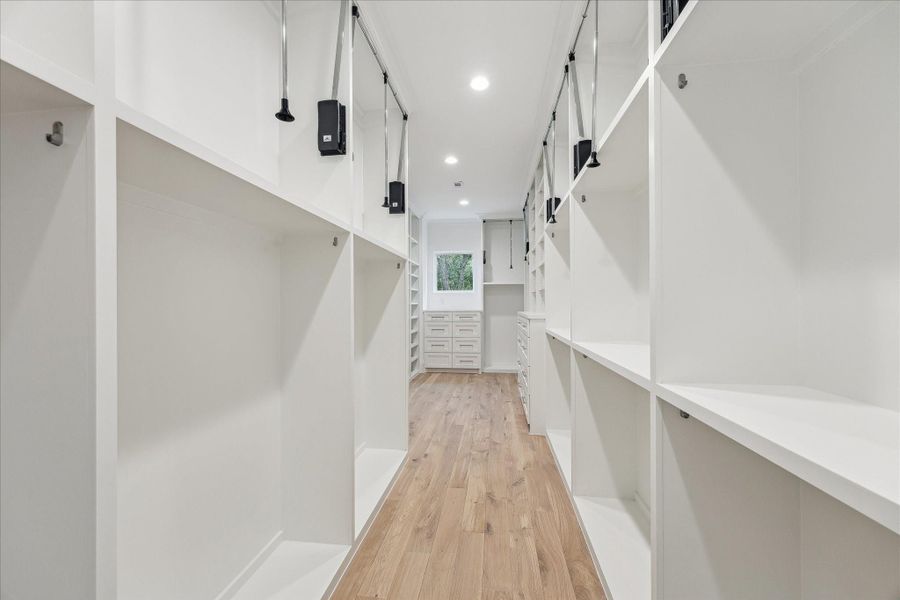 Spacious primary closet features built-in storage and ample room for hanging clothes with pull-down bars for accessing all custom storage solutions.