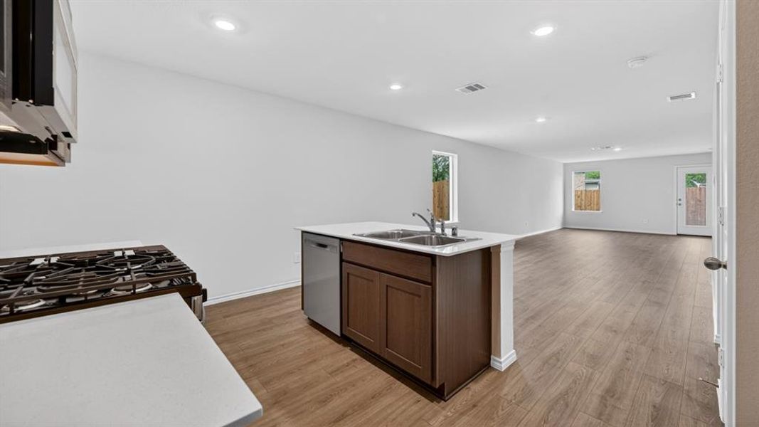 Kitchen island featuring a double basin stainless steel sink, a stainless steel dishwasher, and dark wood cabinetry