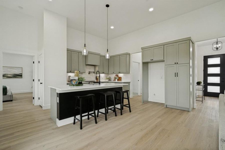 Open-concept kitchen featuring light gray cabinetry, white countertops, and a black kitchen island with pendant lighting Open-concept kitchen featuring light gray cabinetry, white countertops, and a black kitchen island with pendant lighting