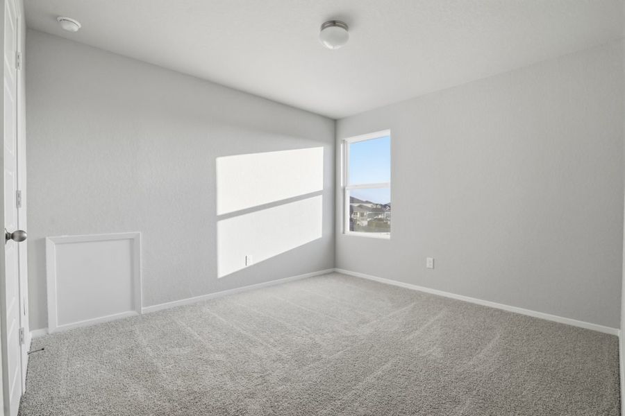 Image of a bedroom with light grey walls, tan carpeting, a window and white trim