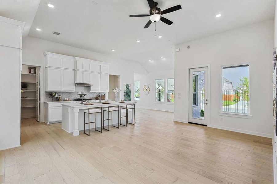 Kitchen with a breakfast bar, light wood-type flooring, an island with sink, white cabinets, and ceiling fan