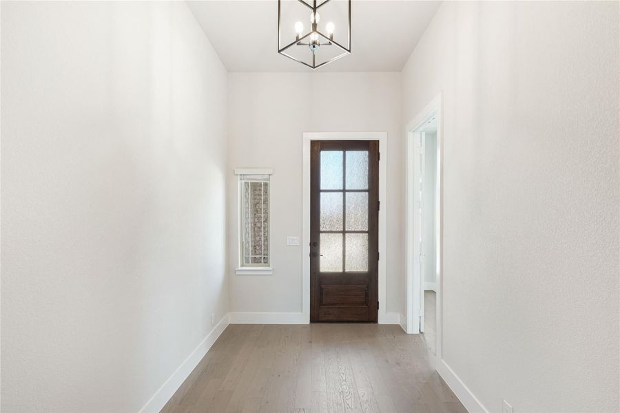 Entryway with dark wood glass-panel front door, hardwood floors, and geometric pendant light fixture. Entryway with dark wood glass-panel front door, hardwood floors, and geometric pendant light fixture.
