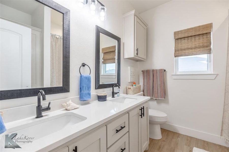 Full bath featuring light wood-type flooring, double vanity, and a shower with shower curtain Full bath featuring light wood-type flooring, double vanity, and a shower with shower curtain