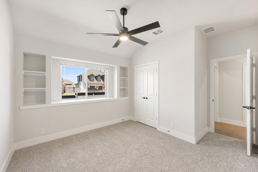 Empty bedroom with carpet, vaulted ceiling, ceiling fan, built-in shelves, and closet door