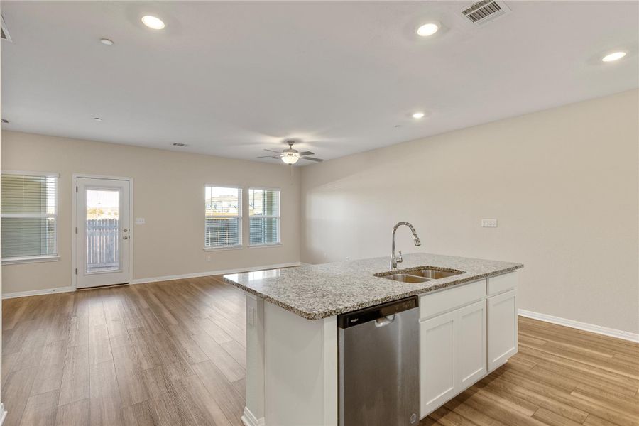 Kitchen/Living View featuring stainless steel dishwasher, open floor plan, light wood-type flooring, light stone counters, and a kitchen island with sink Kitchen/Living View featuring stainless steel dishwasher, open floor plan, light wood-type flooring, light stone counters, and a kitchen island with sink