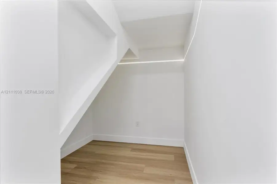 Architectural alcove featuring wood-finish flooring, smooth white walls, and integrated linear LED strip lighting
