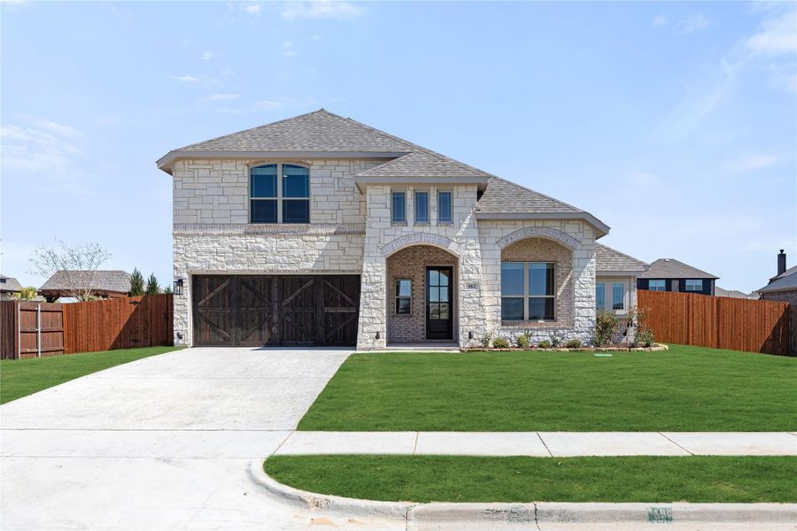 Two-story home with stone and brick exterior, two-car garage with wood doors, and manicured front lawn