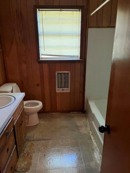 Bathroom featuring wood-paneled walls, a window with blinds, and a wall-mounted heater Bathroom featuring wood-paneled walls, a window with blinds, and a wall-mounted heater