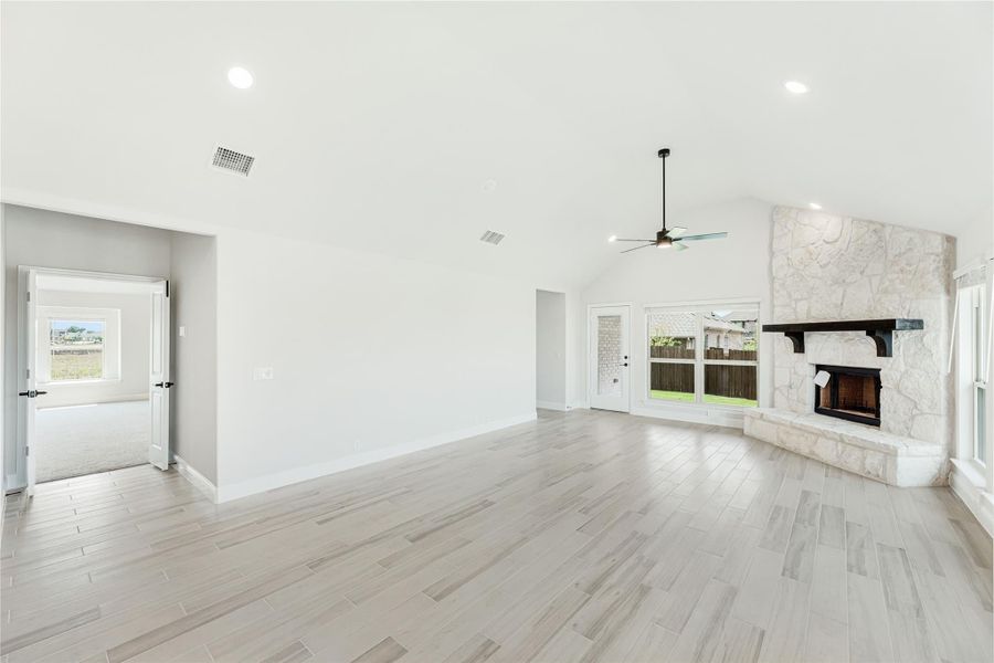 Open living room with vaulted ceiling, stone fireplace, ceiling fan, and light wood-look tile floors