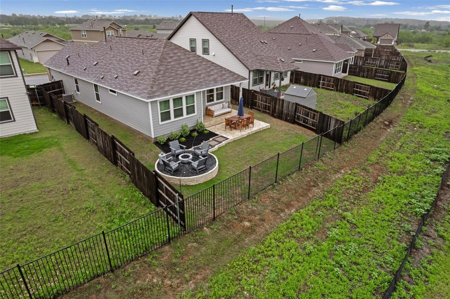 Expansive backyard featuring a stone patio, built-in fire pit, and black wrought iron fencing