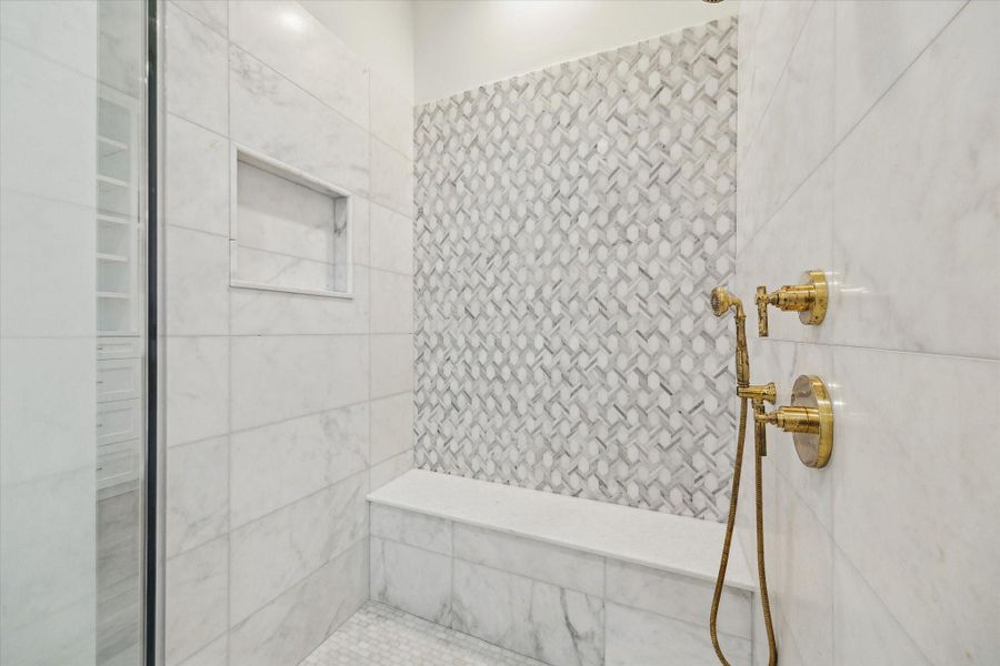 Framed glass shower with mosaic floor, large niche, and bench create a cohesive space.