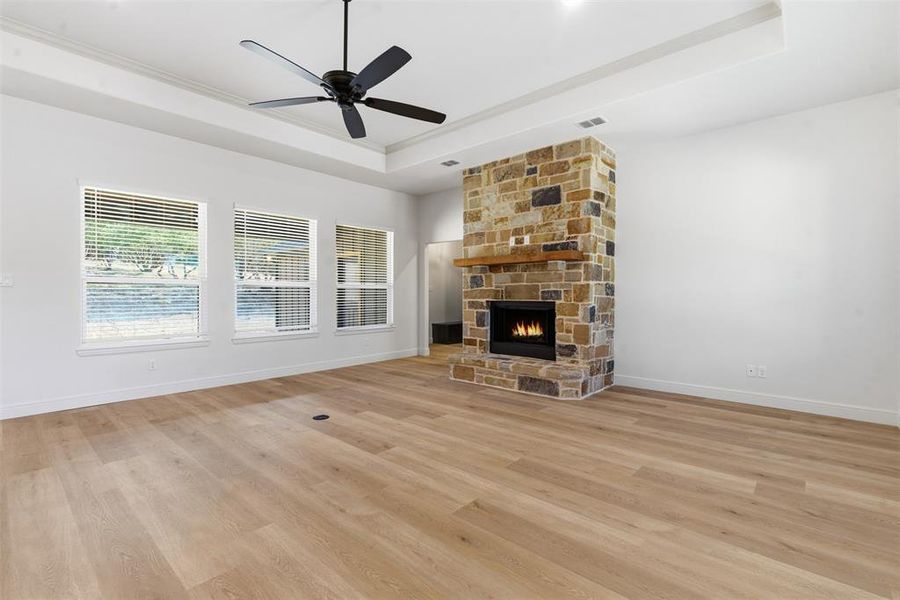Unfurnished living room with a tray ceiling, light wood finished floors, a fireplace, a ceiling fan, and crown molding Unfurnished living room with a tray ceiling, light wood finished floors, a fireplace, a ceiling fan, and crown molding