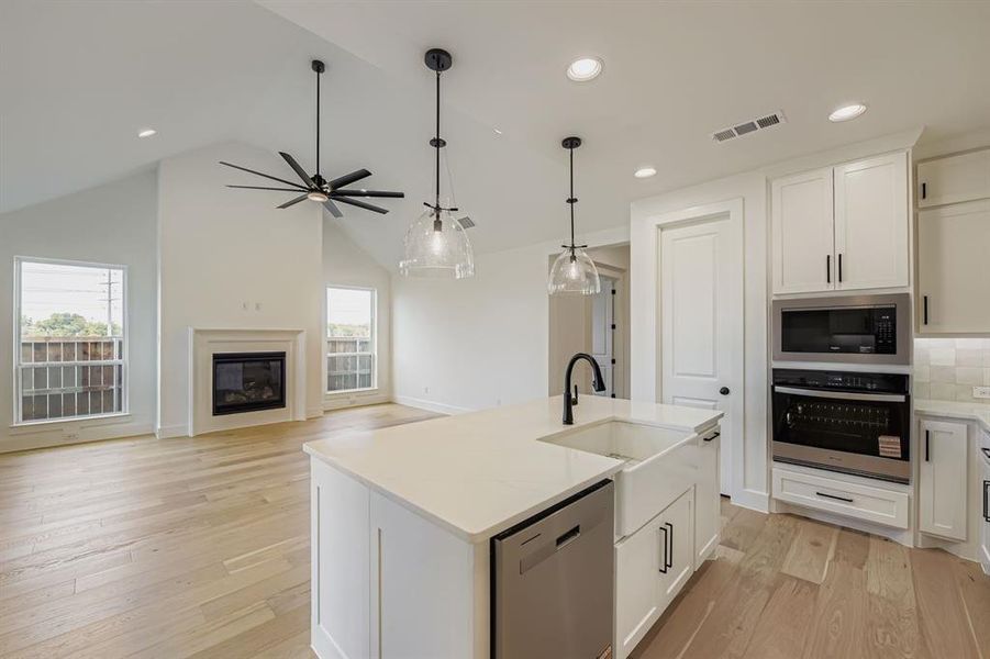Kitchen featuring white cabinets, stainless steel appliances, a center island with sink, ceiling fan, and light wood finished floors Kitchen featuring white cabinets, stainless steel appliances, a center island with sink, ceiling fan, and light wood finished floors