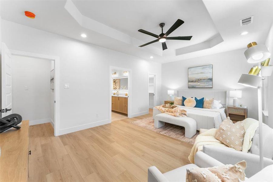 Bedroom with a spacious closet, recessed lighting, light wood finished floors, ceiling fan, and a tray ceiling