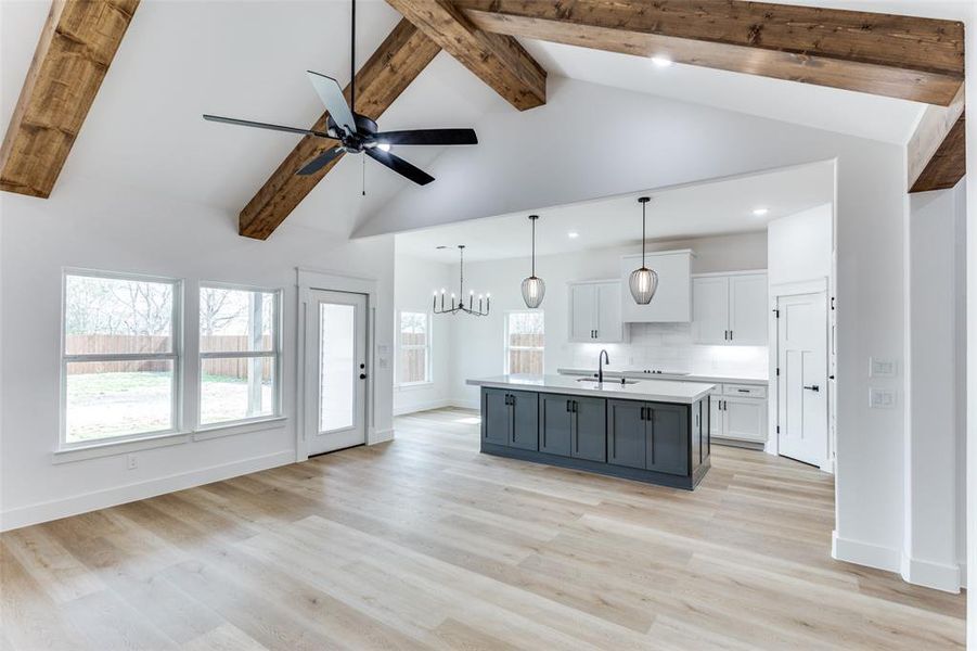 Kitchen featuring white cabinets, a sink, a kitchen island with sink, light countertops, and beam ceiling