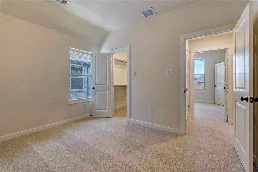 Unfurnished bedroom with light colored carpet, a spacious closet, multiple windows, and vaulted ceiling Unfurnished bedroom with light colored carpet, a spacious closet, multiple windows, and vaulted ceiling