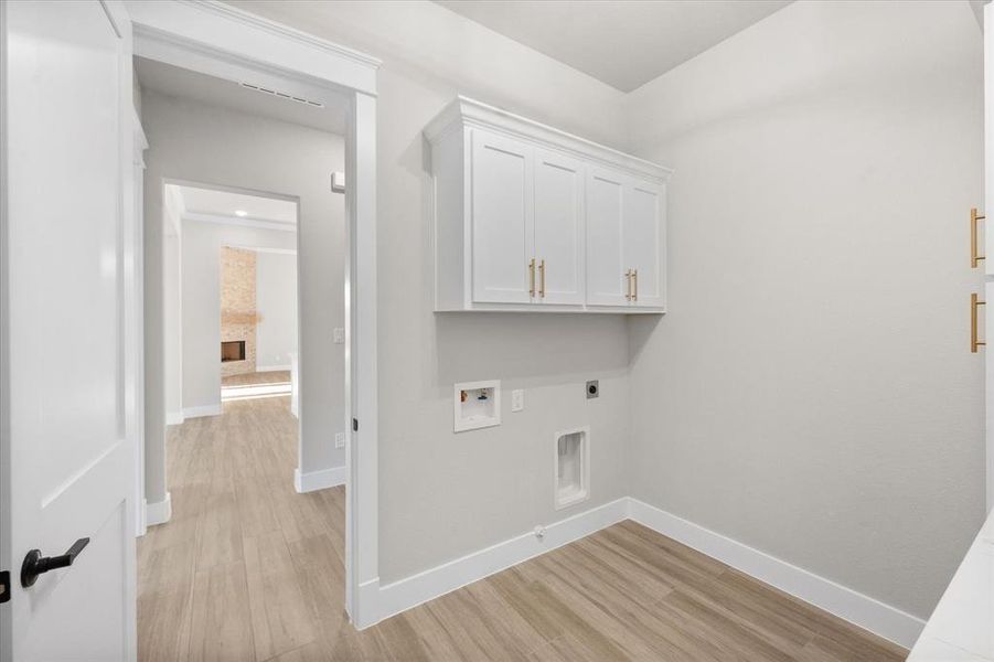 Clothes washing area with hookup for an electric dryer, light wood-type flooring, a fireplace, and hookup for a washing machine