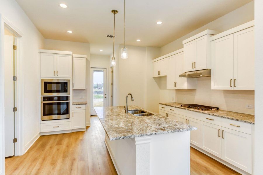 Kitchen with stainless steel appliances, a center island with sink, light wood-style floors, and white cabinets