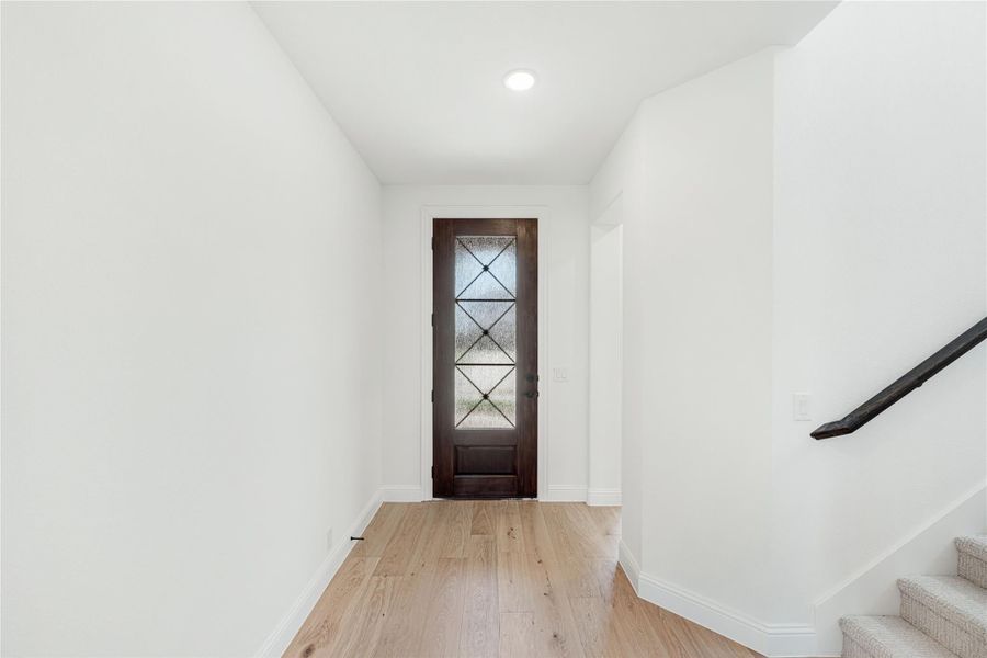 Entryway with dark wood front door, glass panels, light hardwood floors, and staircase with dark handrail
