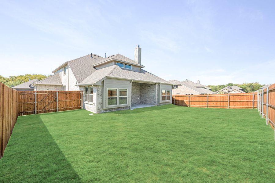 Backyard of brick home with large green lawn, covered patio, and wood privacy fence Backyard of brick home with large green lawn, covered patio, and wood privacy fence