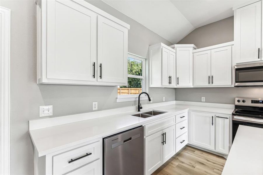 Kitchen featuring stainless steel appliances, sink, lofted ceiling, light wood-type flooring, and white cabinets