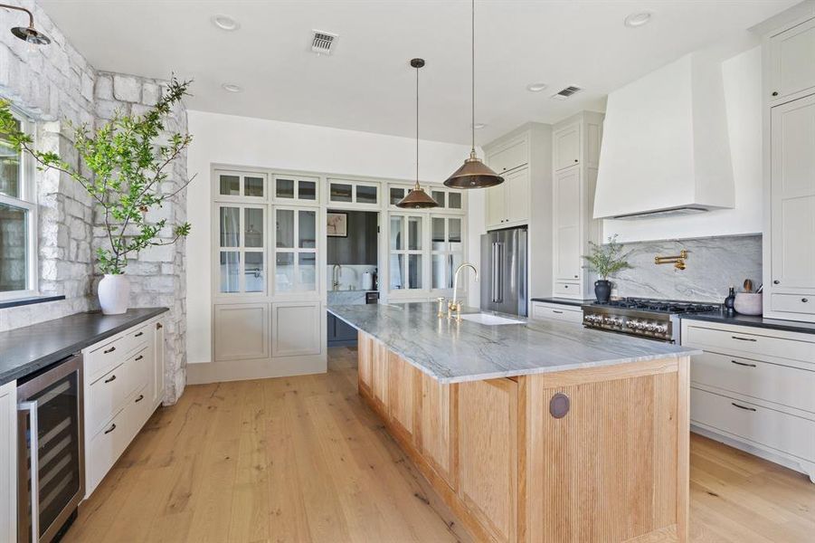 Kitchen featuring light hardwood / wood-style flooring, beverage cooler, custom exhaust hood, an island with sink, and premium appliances