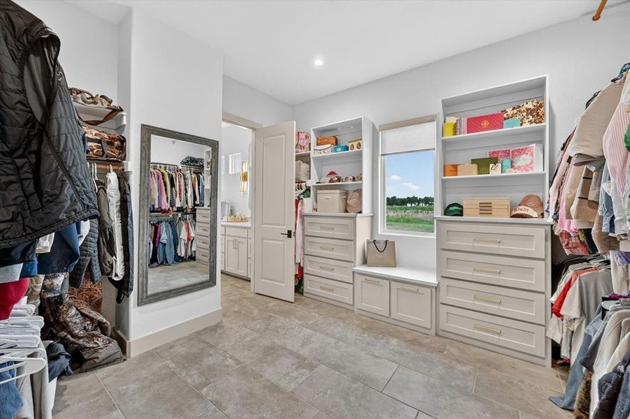 Spacious walk-in closet featuring extensive built-in cabinetry, integrated shelving, a full-length mirror, and tile flooring