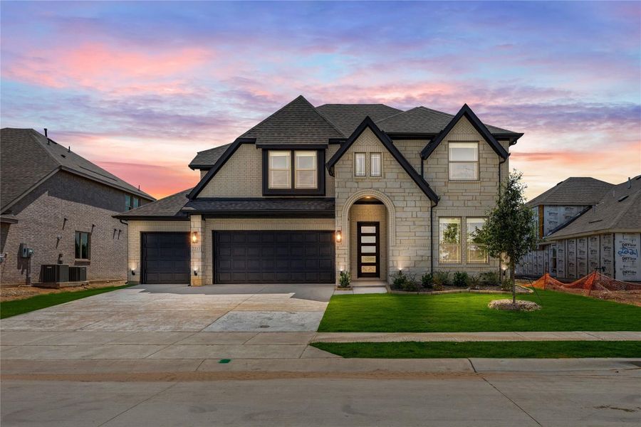 Two-story stone home with three-car garage, arched entry, and dark roof at dusk