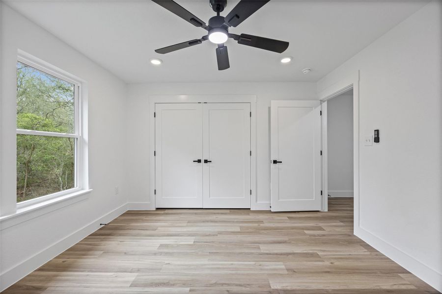 Bright room featuring light wood-finish flooring, a contemporary black ceiling fan with integrated lighting, recessed ceiling lights, and white walls with thick baseboards Bright room featuring light wood-finish flooring, a contemporary black ceiling fan with integrated lighting, recessed ceiling lights, and white walls with thick baseboards