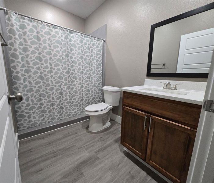 Full bathroom featuring a wood-finish vanity with a light-toned countertop, a built-in sink with a chrome faucet, and a wall-mounted mirror with a black frame