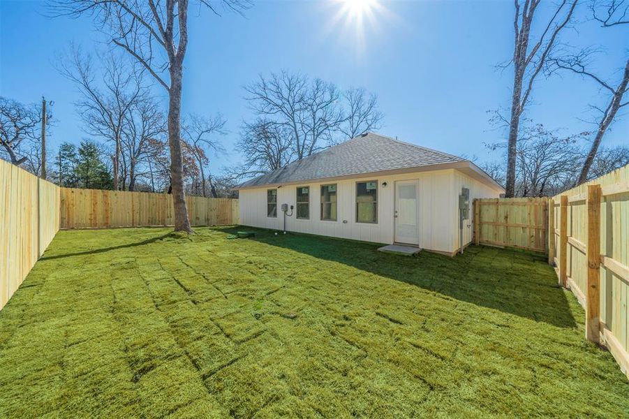 Rear view of property with a shingled roof, a lawn, and a fenced backyard