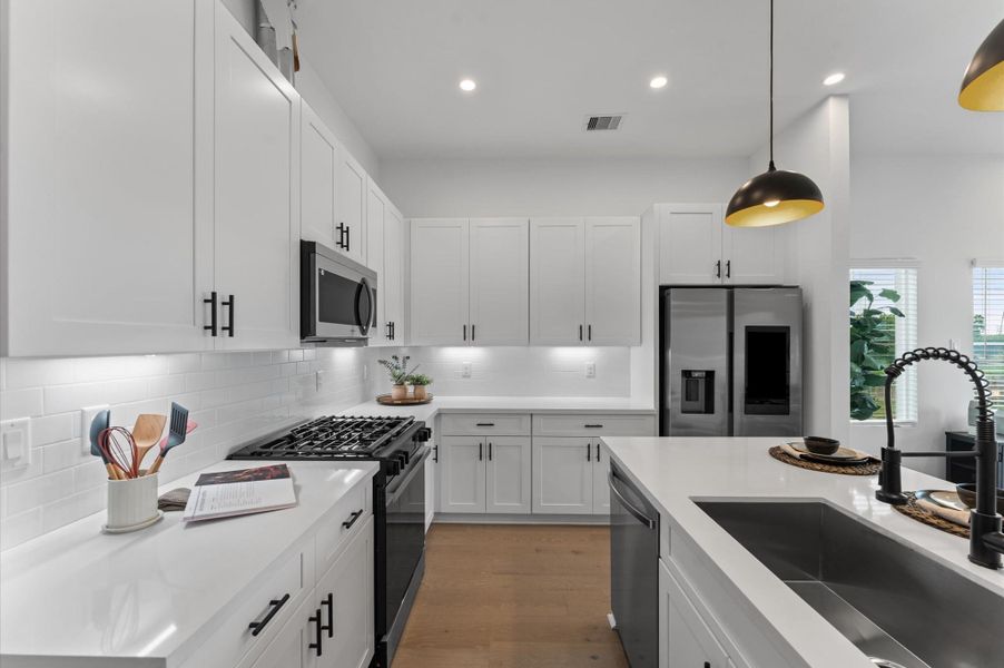 This modern kitchen is a masterclass in both style and functionality, featuring abundant cabinetry along the walls and a spacious island with built-in storage. The cabinetry offers generous room for cookware, pantry items, and small appliances, while the island includes drawers and cabinets that maximize organization and prep space. Sleek stainless-steel appliances, blend seamlessly into the design, enhancing the kitchen’s polished aesthetic.