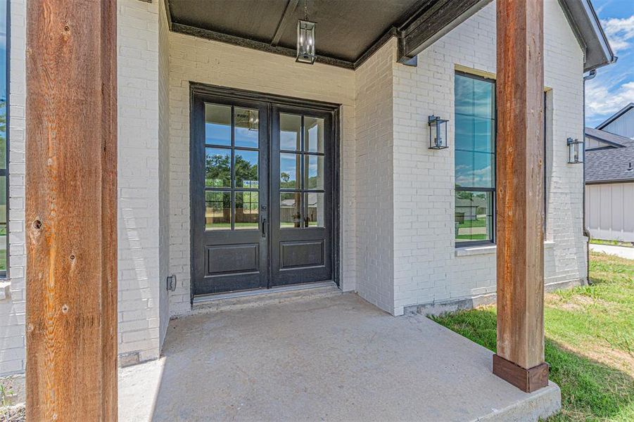 Entryway featuring double black French doors, white brick exterior, natural wood-finish support columns, and black exterior light fixtures
