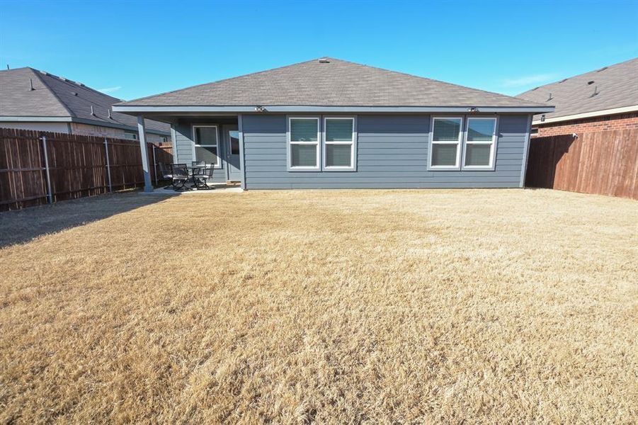 Back of property featuring roof with shingles, a fenced backyard, a lawn, and a patio