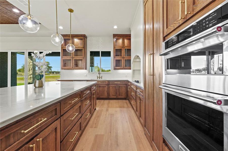 Kitchen featuring stainless steel double oven, hanging light fixtures, light wood finished floors, recessed lighting, and brown cabinets Kitchen featuring stainless steel double oven, hanging light fixtures, light wood finished floors, recessed lighting, and brown cabinets