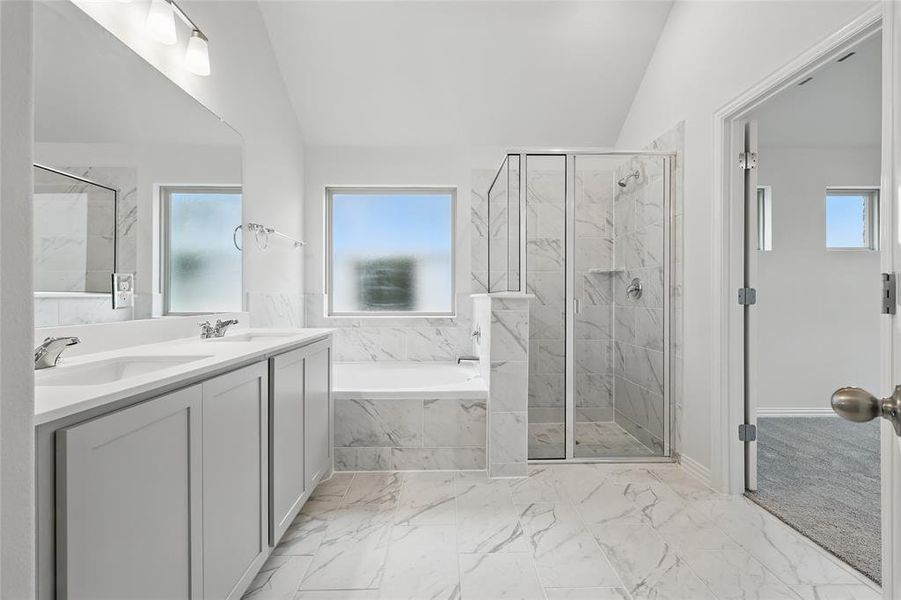 Full bath featuring a marble finish shower, vaulted ceiling, light marble finish flooring, double vanity, and a bath