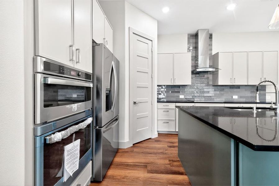 Kitchen with stainless steel appliances, dark wood-style flooring, white cabinetry, dark stone countertops, and tasteful backsplash Kitchen with stainless steel appliances, dark wood-style flooring, white cabinetry, dark stone countertops, and tasteful backsplash