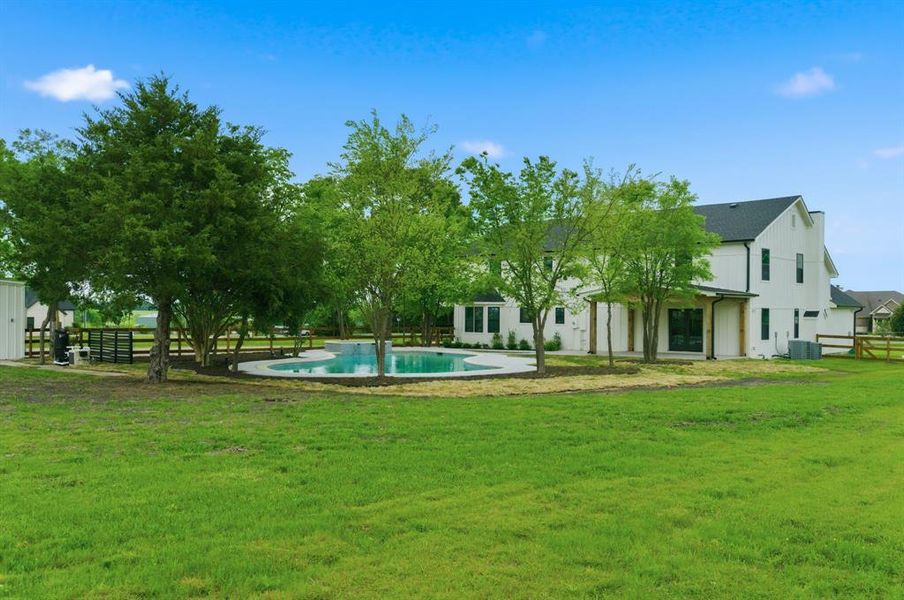 The property features a spacious yard with a lush green lawn and mature trees, alongside a swimming pool with a paved surround The property features a spacious yard with a lush green lawn and mature trees, alongside a swimming pool with a paved surround