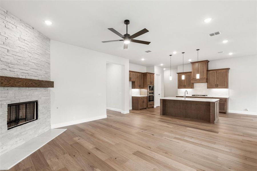 Open living area with stone fireplace, hardwood floors, and kitchen with wood cabinets and large island