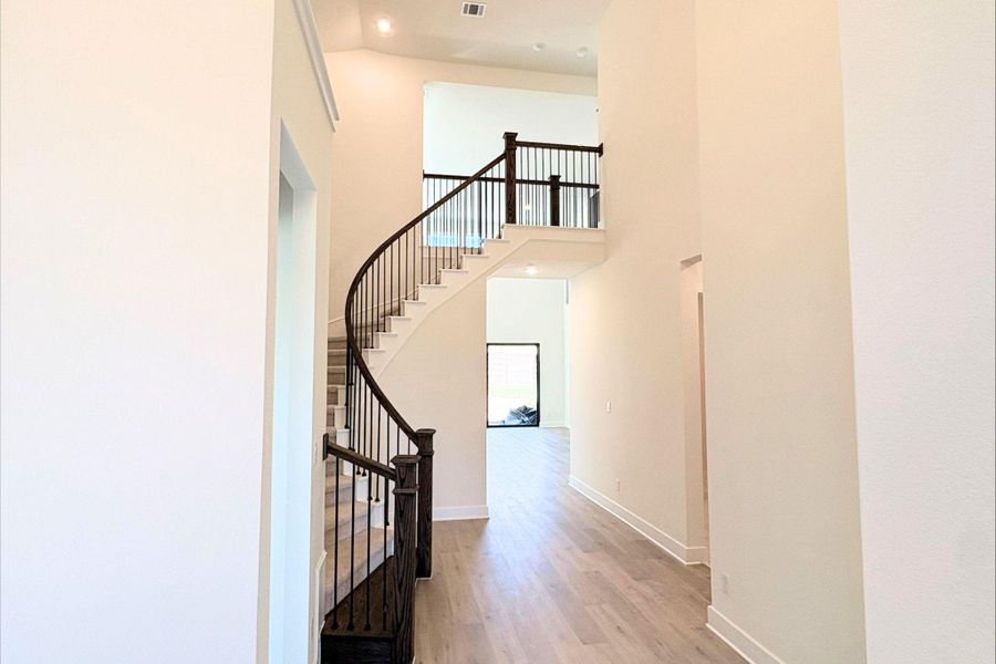 An elegant curved staircase anchors the soaring foyer entry with sleek wood flooring. An elegant curved staircase anchors the soaring foyer entry with sleek wood flooring.