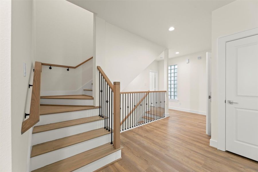 This photo showcases a bright and inviting entryway with a modern staircase featuring sleek black railings. The space has warm  flooring, neutral walls, and recessed lighting, creating a clean and contemporary look.