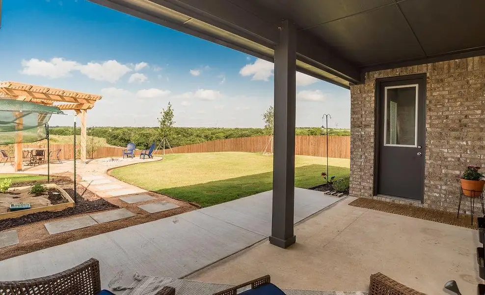 Expansive backyard featuring a covered patio extended to a wooden pergola living space, vegetable garden, a large grassy area, and a privacy fence.