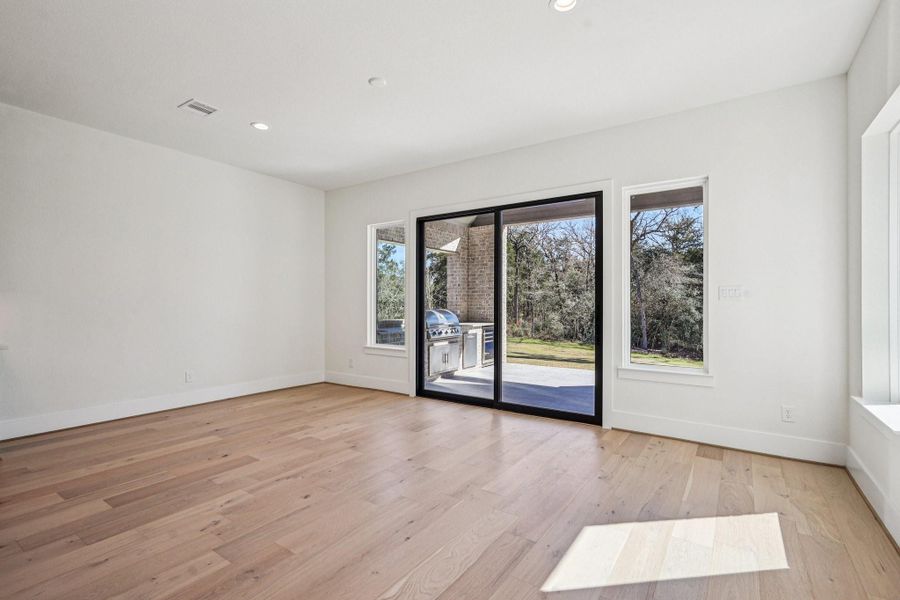 Bright and spacious dining room with light wood floors, large sliding glass doors, and windows offering a view of a lush backyard. Ideal for indoor-outdoor living.