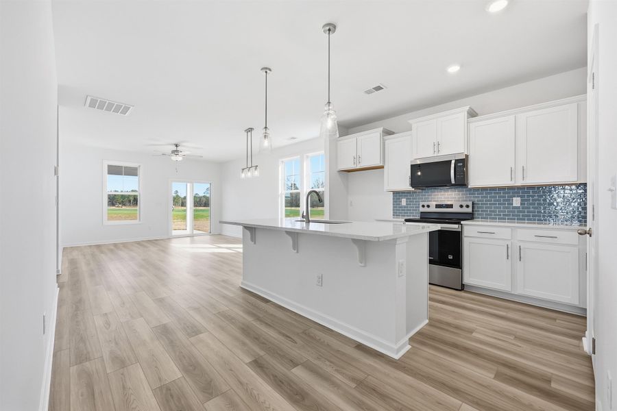 Kitchen featuring a kitchen bar, appliances with stainless steel finishes, white cabinetry, decorative light fixtures, and decorative backsplash Kitchen featuring a kitchen bar, appliances with stainless steel finishes, white cabinetry, decorative light fixtures, and decorative backsplash